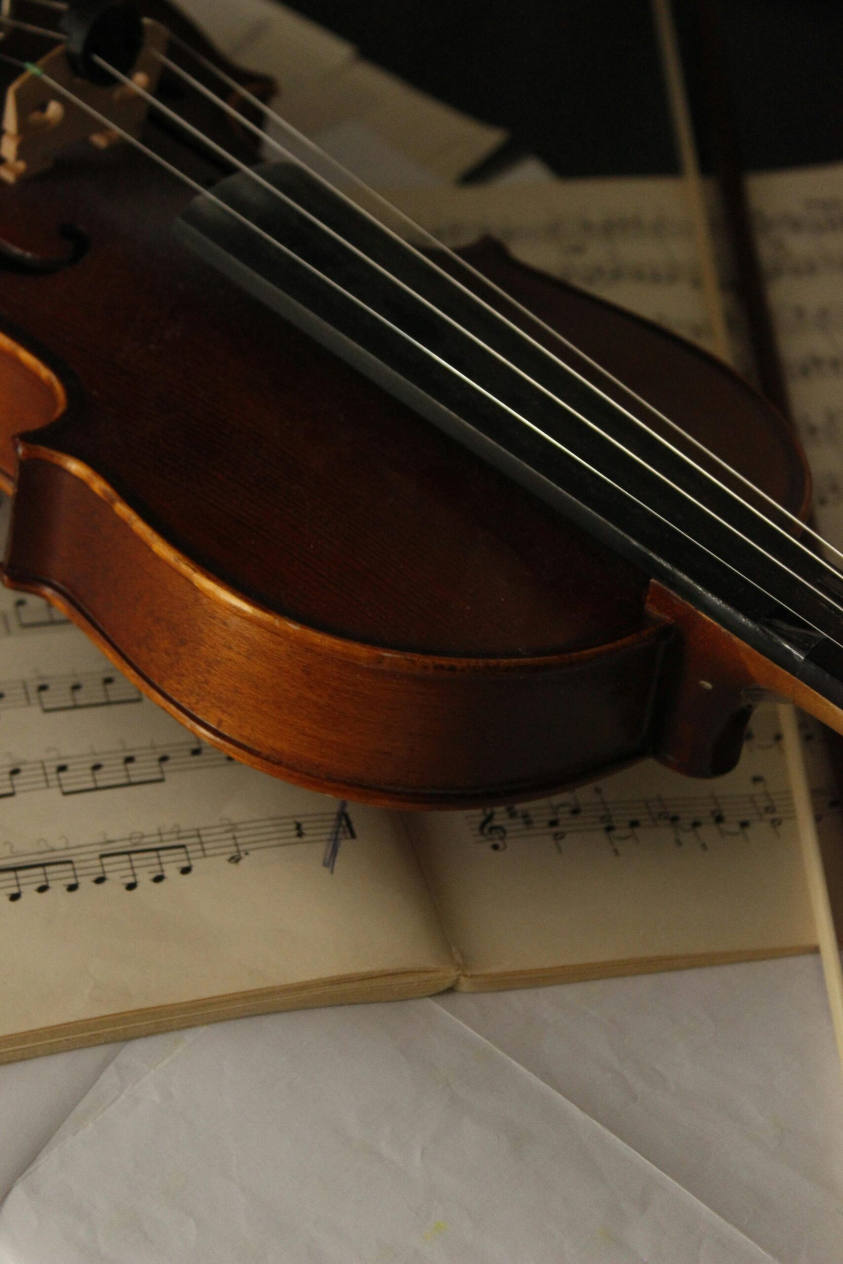 Home A close-up shot of a violin resting on sheet music, displaying warm tones.